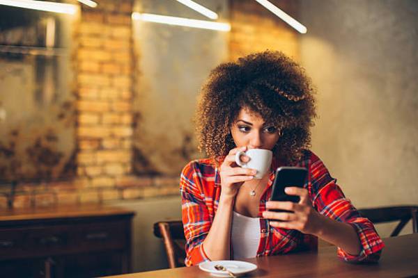 A girl reads a book on her phone over a cup of coffee