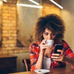 A girl reads a book on her phone over a cup of coffee