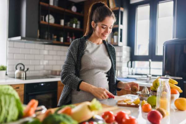 A pregnant woman in the kitchen prepares food for a meal