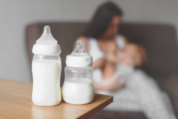 Mom breastfeeds in pregnancy and two bottles of milk for the baby on the table