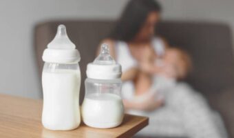 Mom breastfeeds in pregnancy and two bottles of milk for the baby on the table