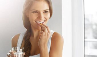 A smiling woman puts nutrilite vitamin in her mouth