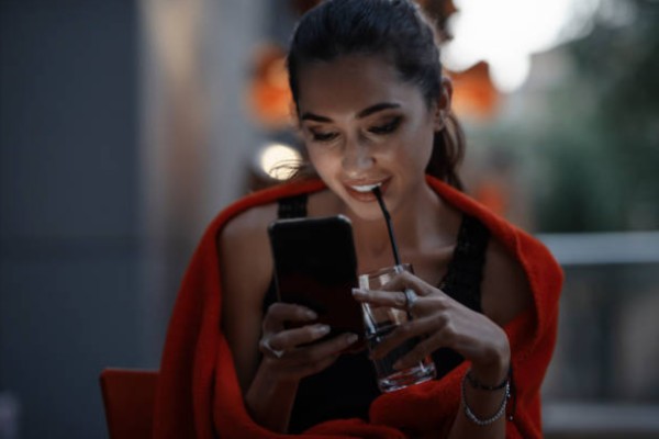 A woman on the terrace of the café looks at the partner search app on the phone