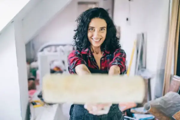A smiling woman holds a whitewash roller