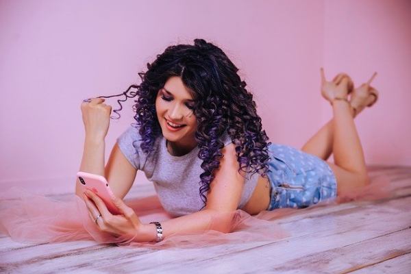 A woman is lying on the bed and looking at her cell phone for a match on a dating app