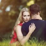 A couple in love sit in a meadow hugging each other